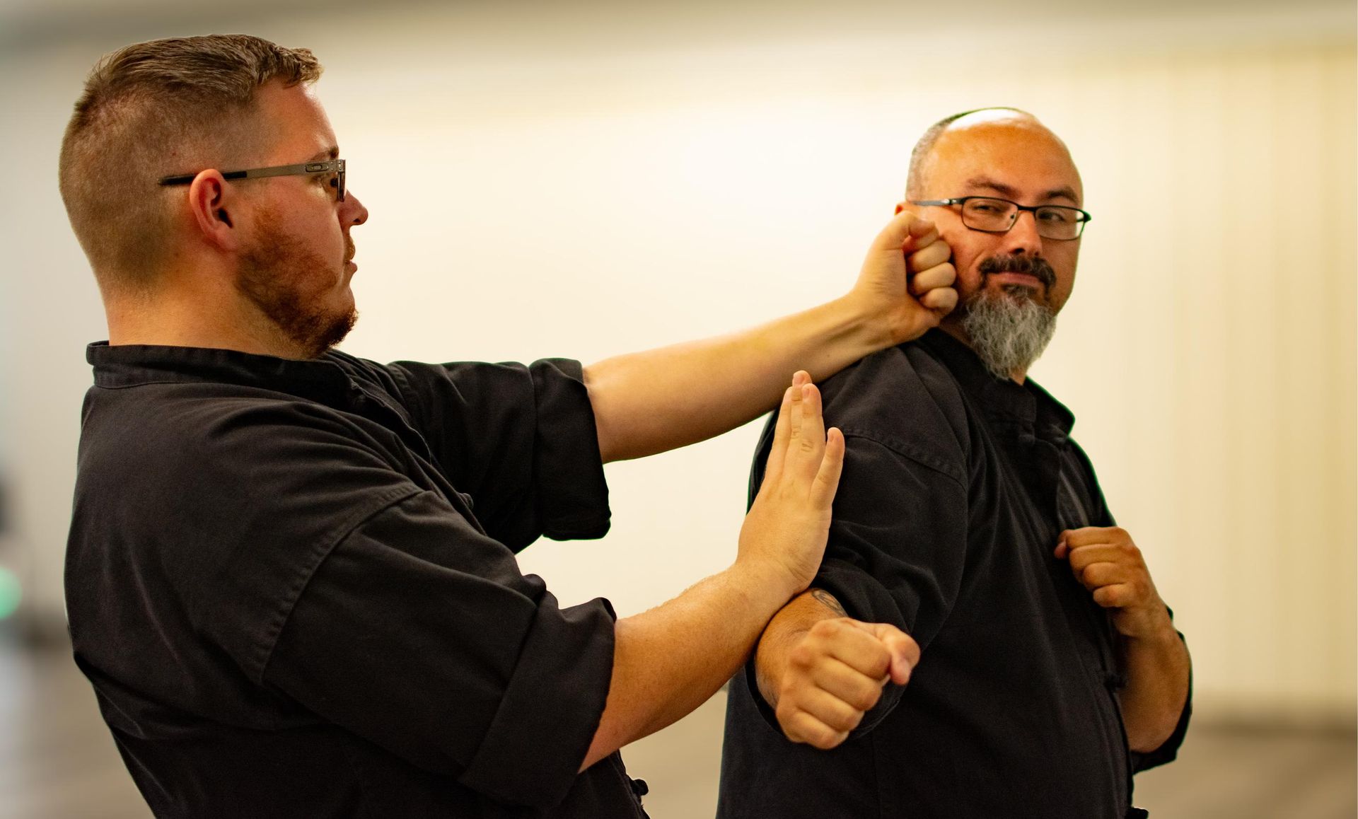 Two men practicing martial arts, one blocking a punch in a bright room.