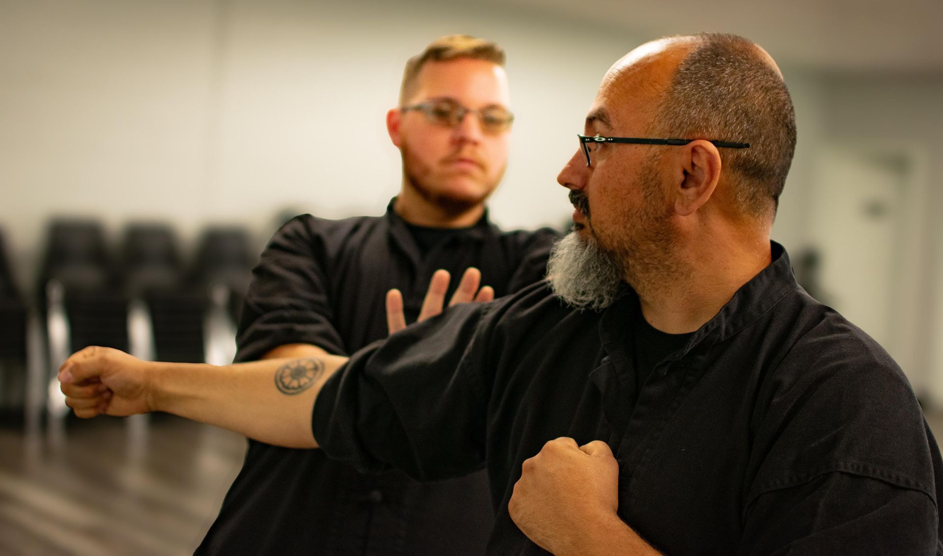 Two men in black martial arts uniforms practicing in a studio. One punches; the other blocks.