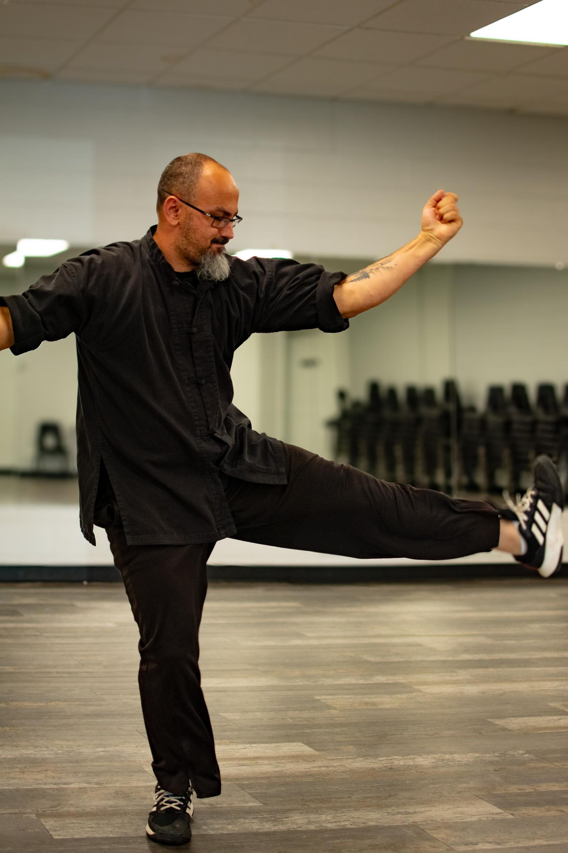 Man in black uniform performs a martial arts kick in a studio with a mirror.