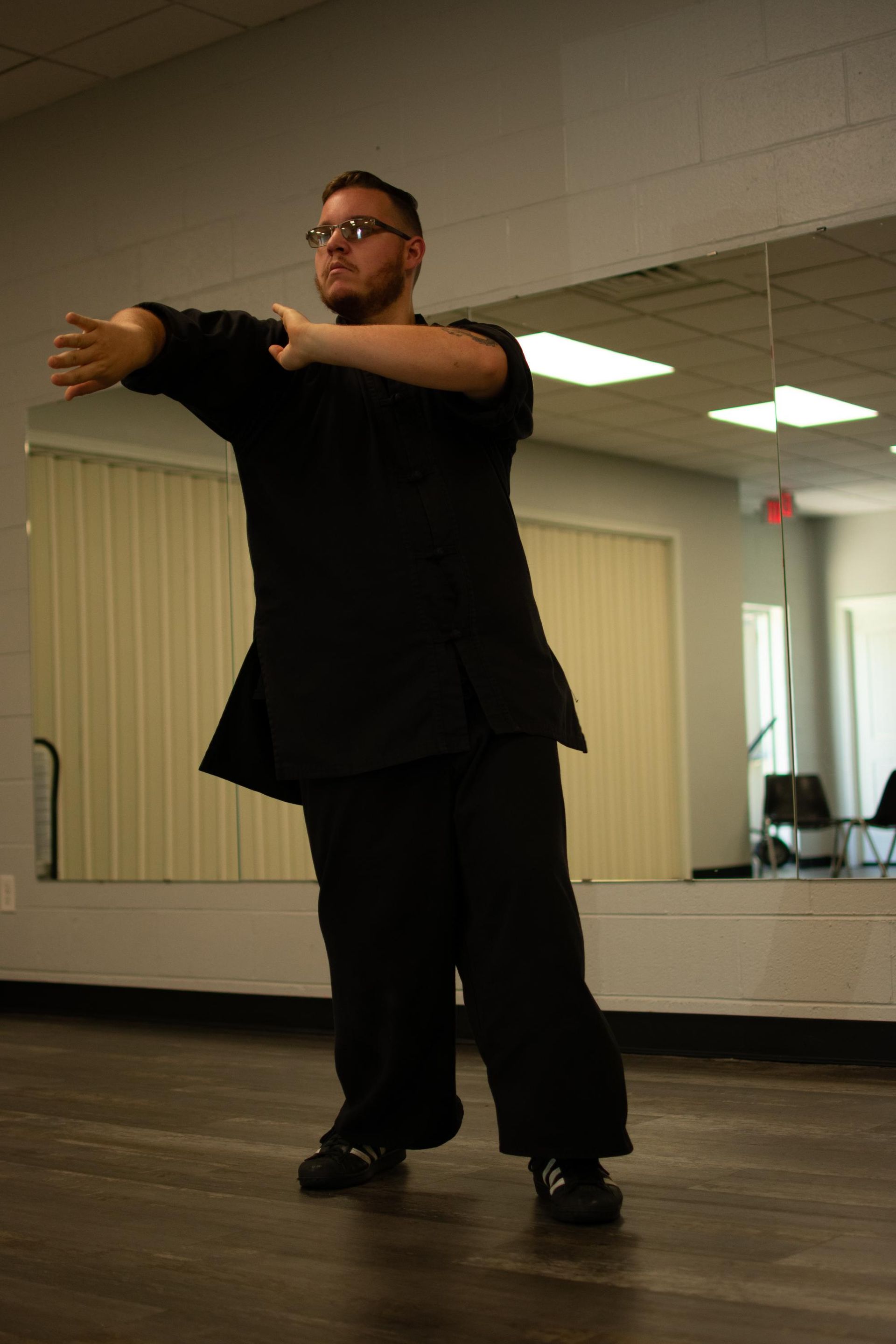 Man in black clothes dancing in a studio, arms outstretched.