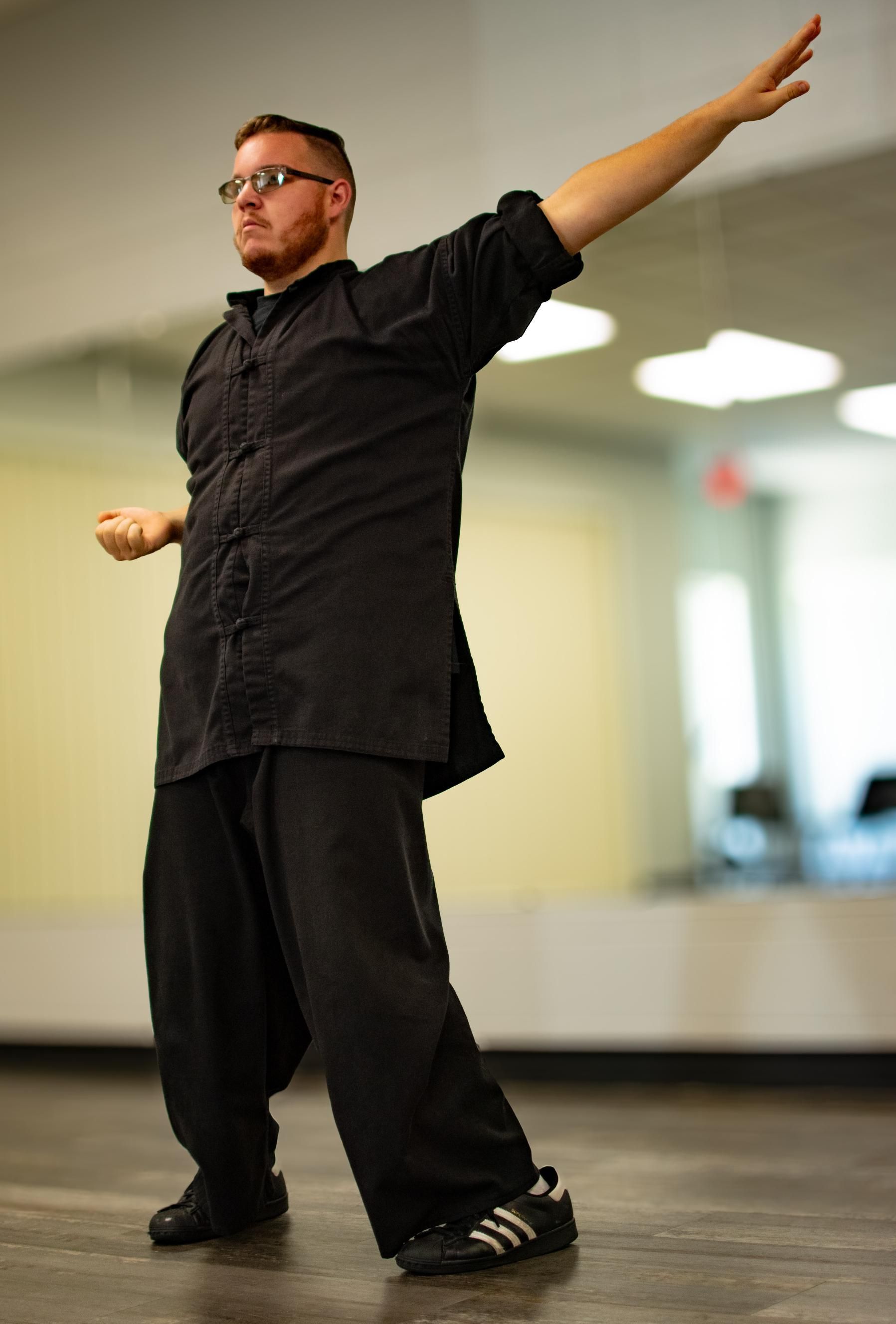Man in black martial arts uniform, arms outstretched, practicing in a dance studio.