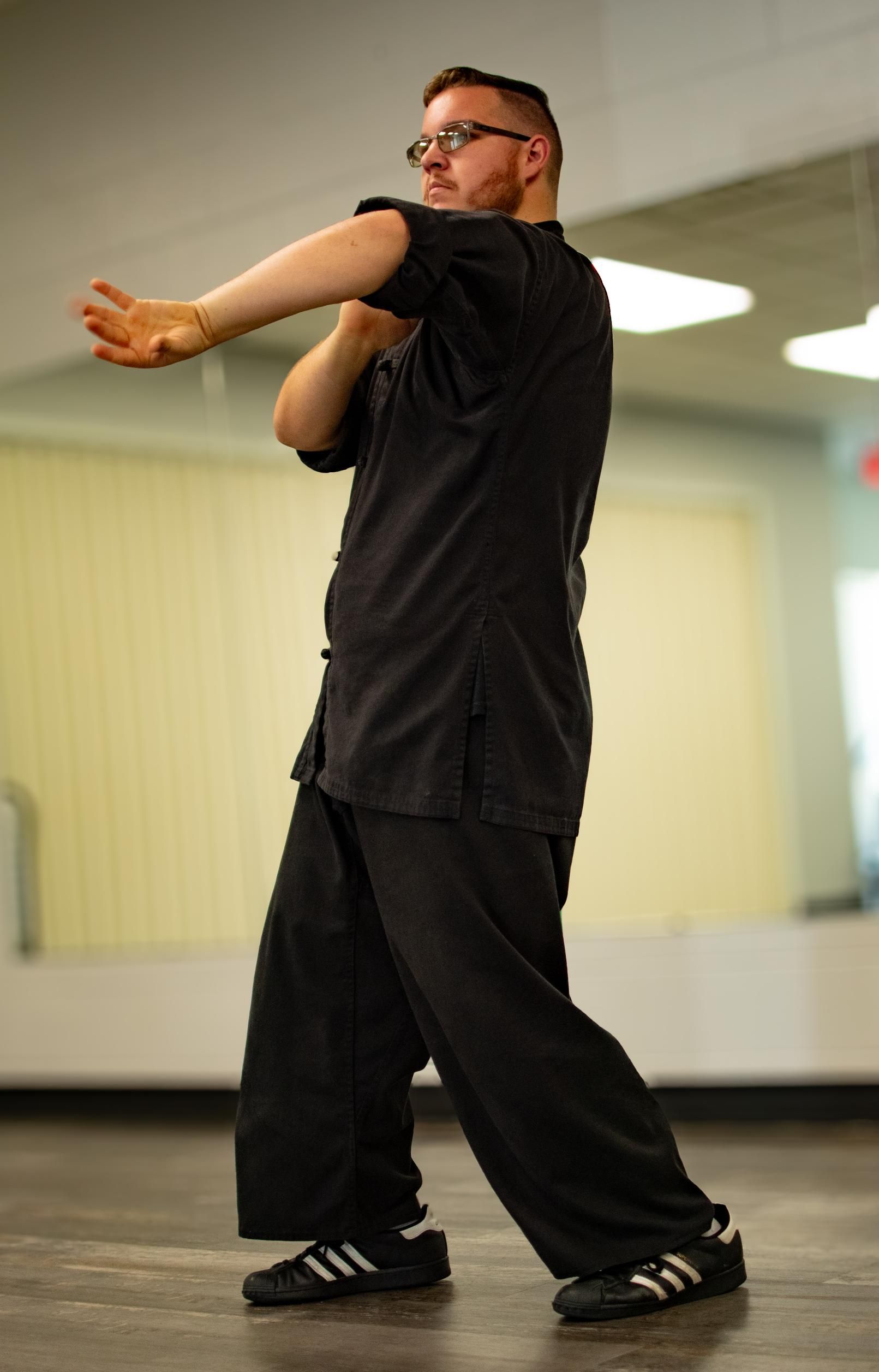 Man in black martial arts uniform, performing a strike, indoor setting.