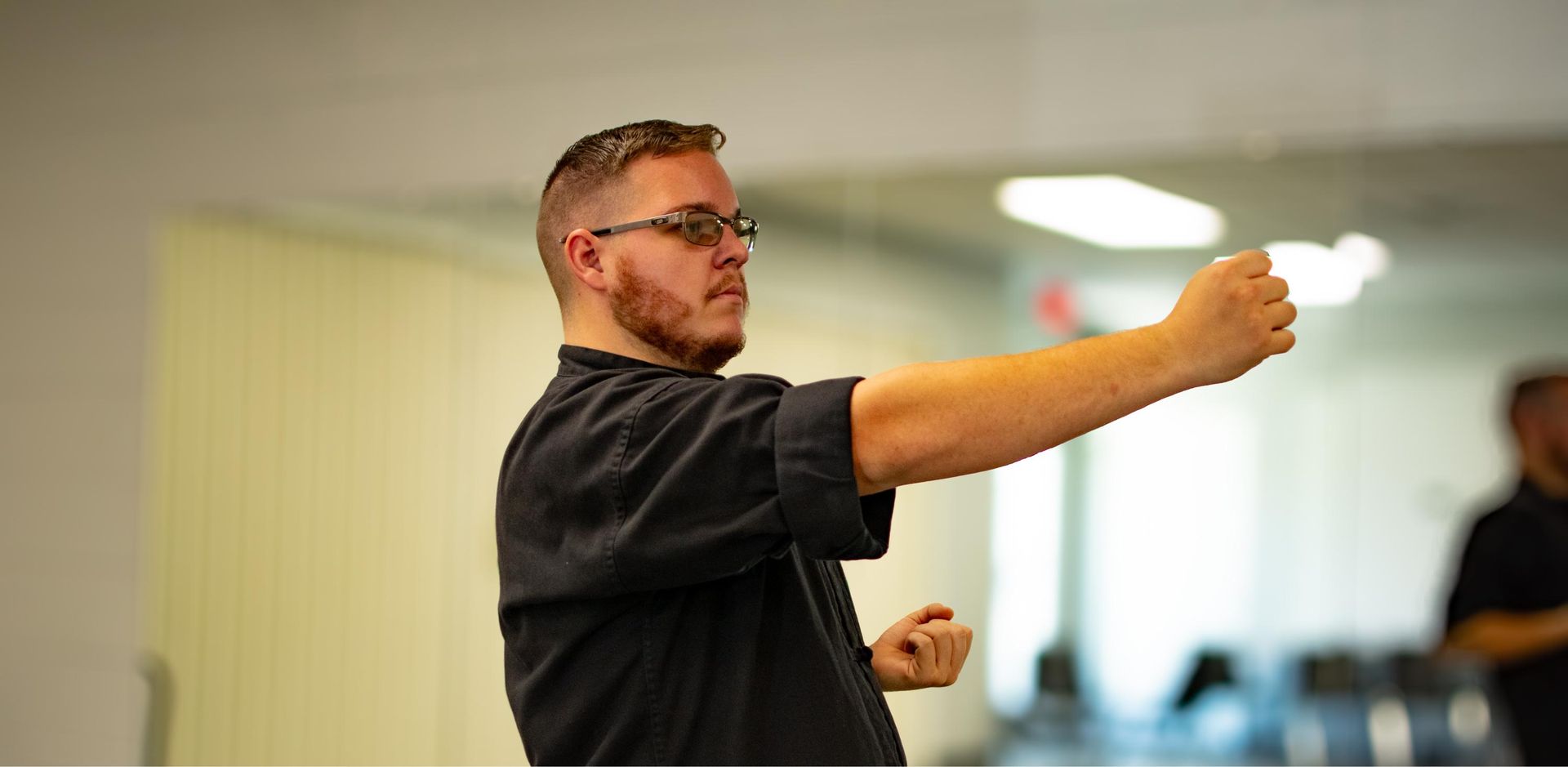 A man in a black shirt practicing a martial art indoors with a clenched fist extended.