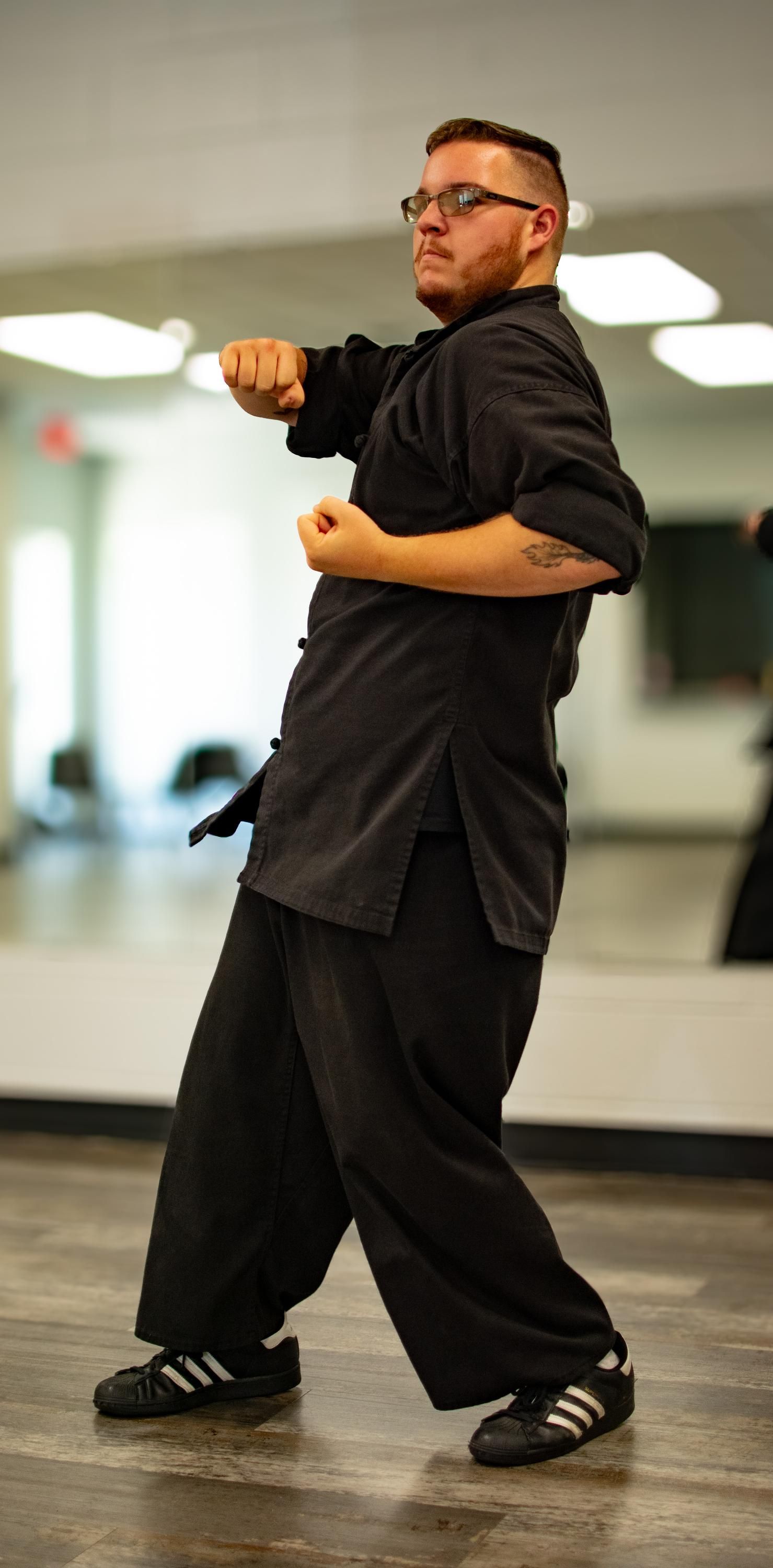 A man in black martial arts uniform performs a punch in a training room.