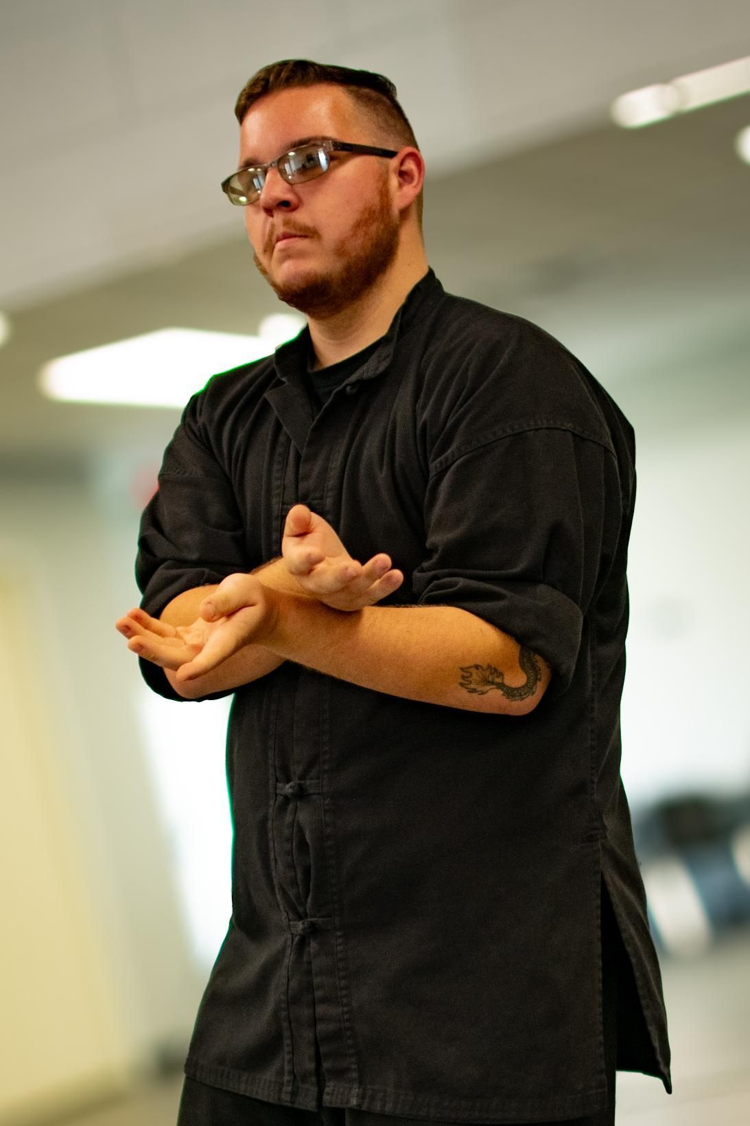 Man with glasses, beard, and black shirt in a martial arts stance, indoors.