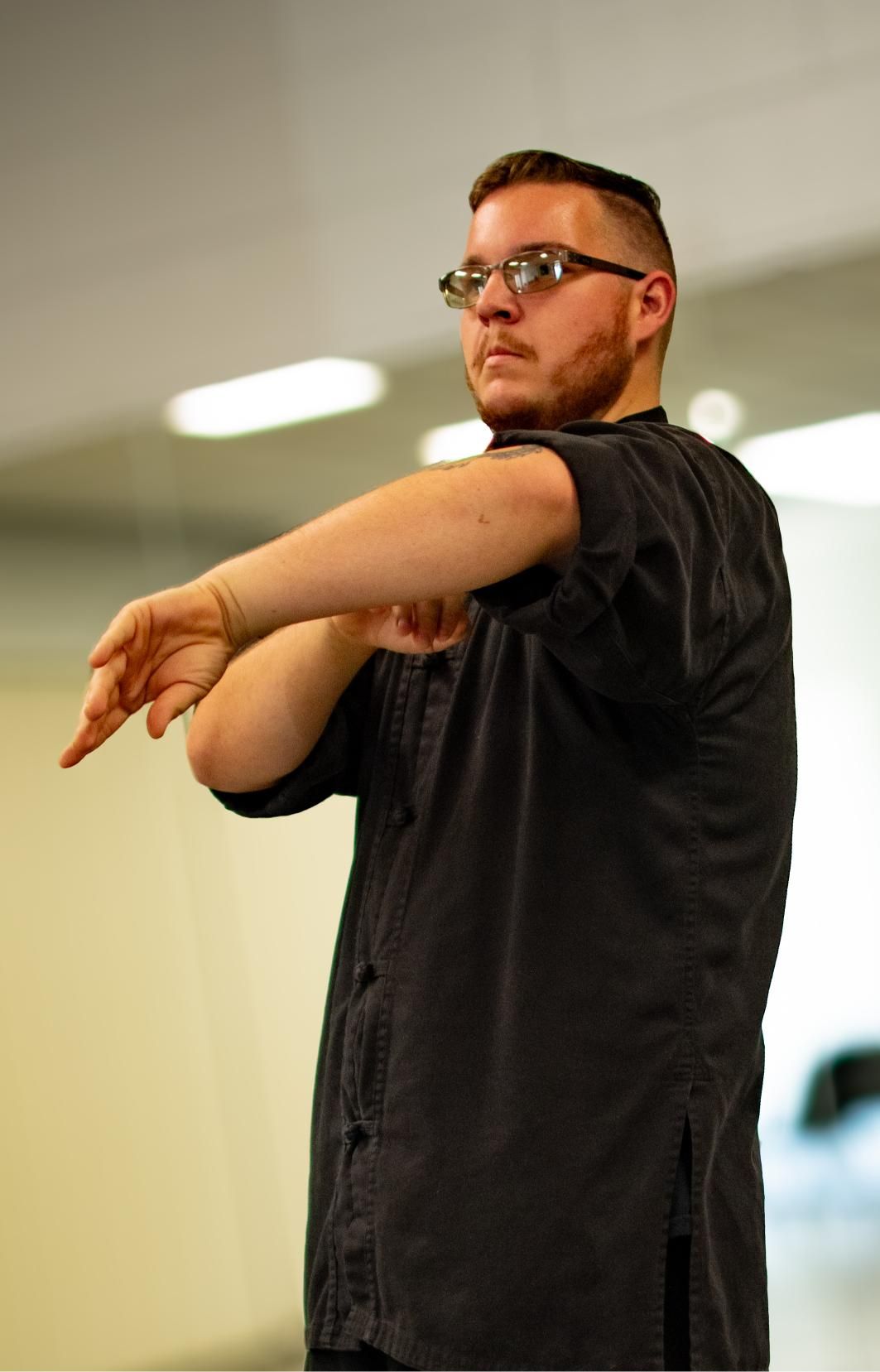 Man with glasses and beard stretches his arm in a hallway.