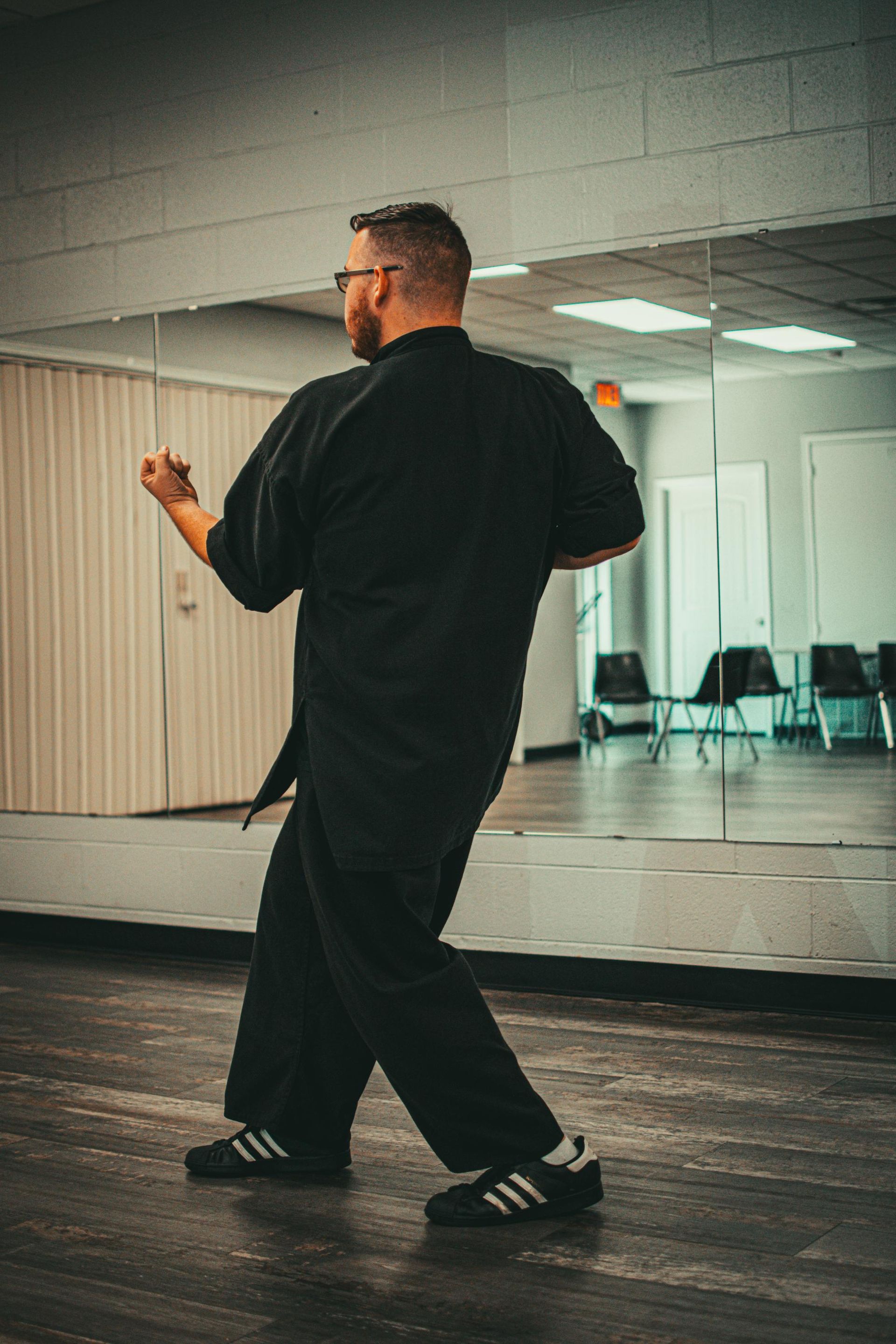 Man in black uniform practices martial arts, standing in front of a mirror.