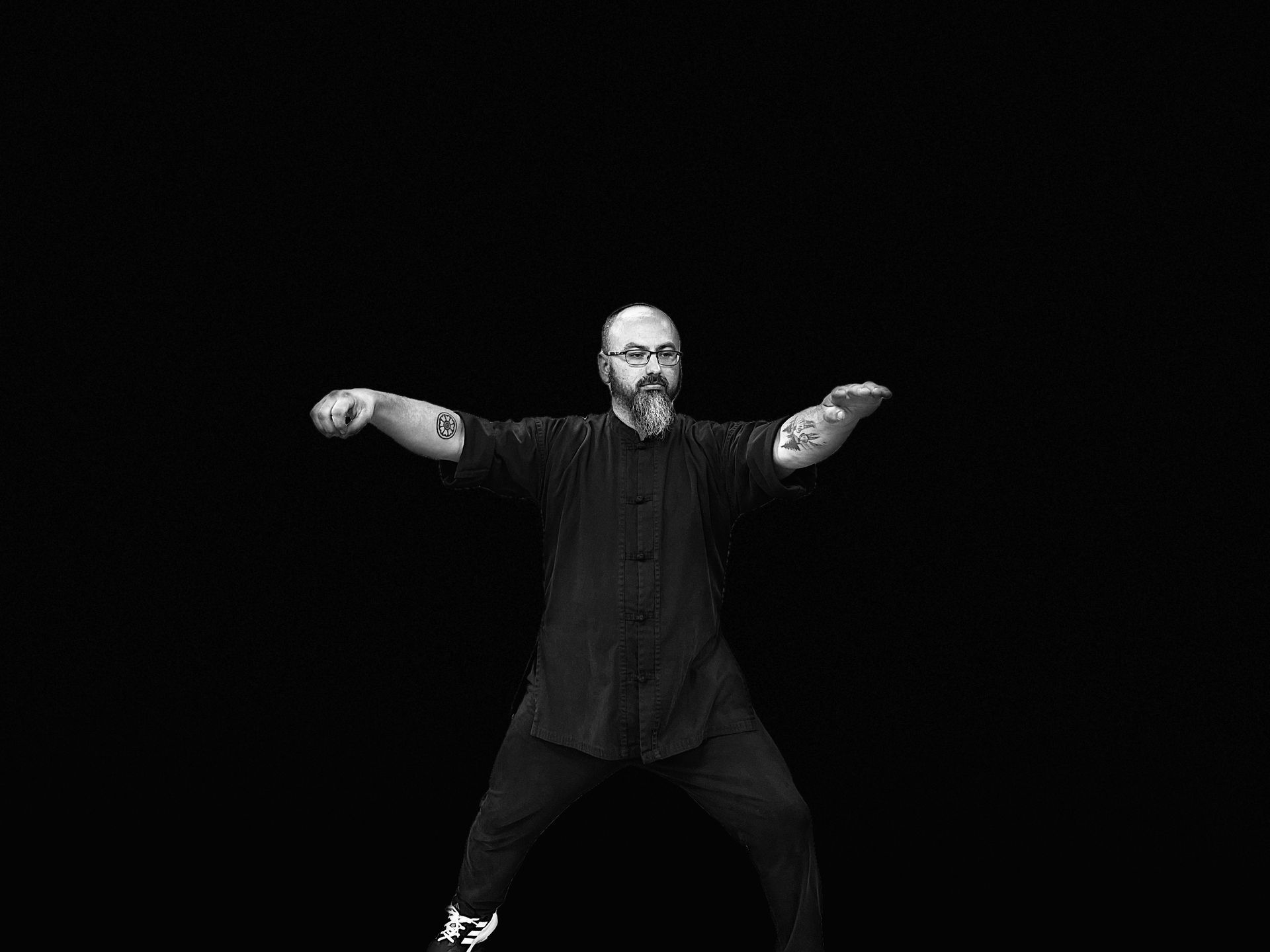 A man with a beard and glasses is dancing in a black and white photo.