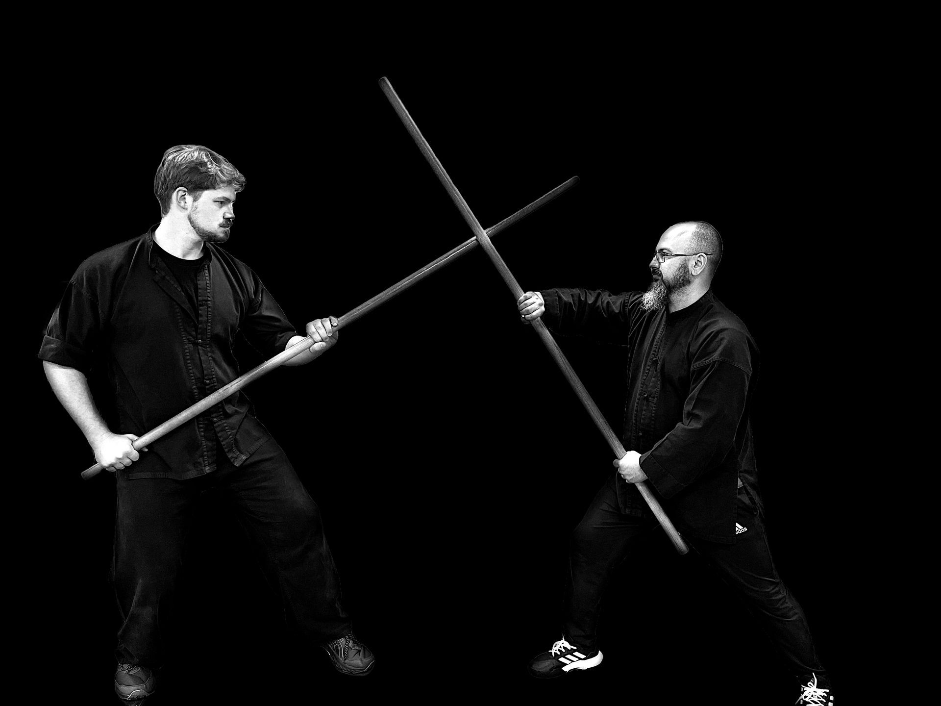 Two men sparring with bo staffs in martial arts stances.