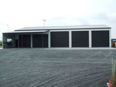 A large building with black garage doors is sitting in a gravel lot.