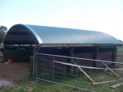 A metal building with a curved roof is sitting in the middle of a grassy field.