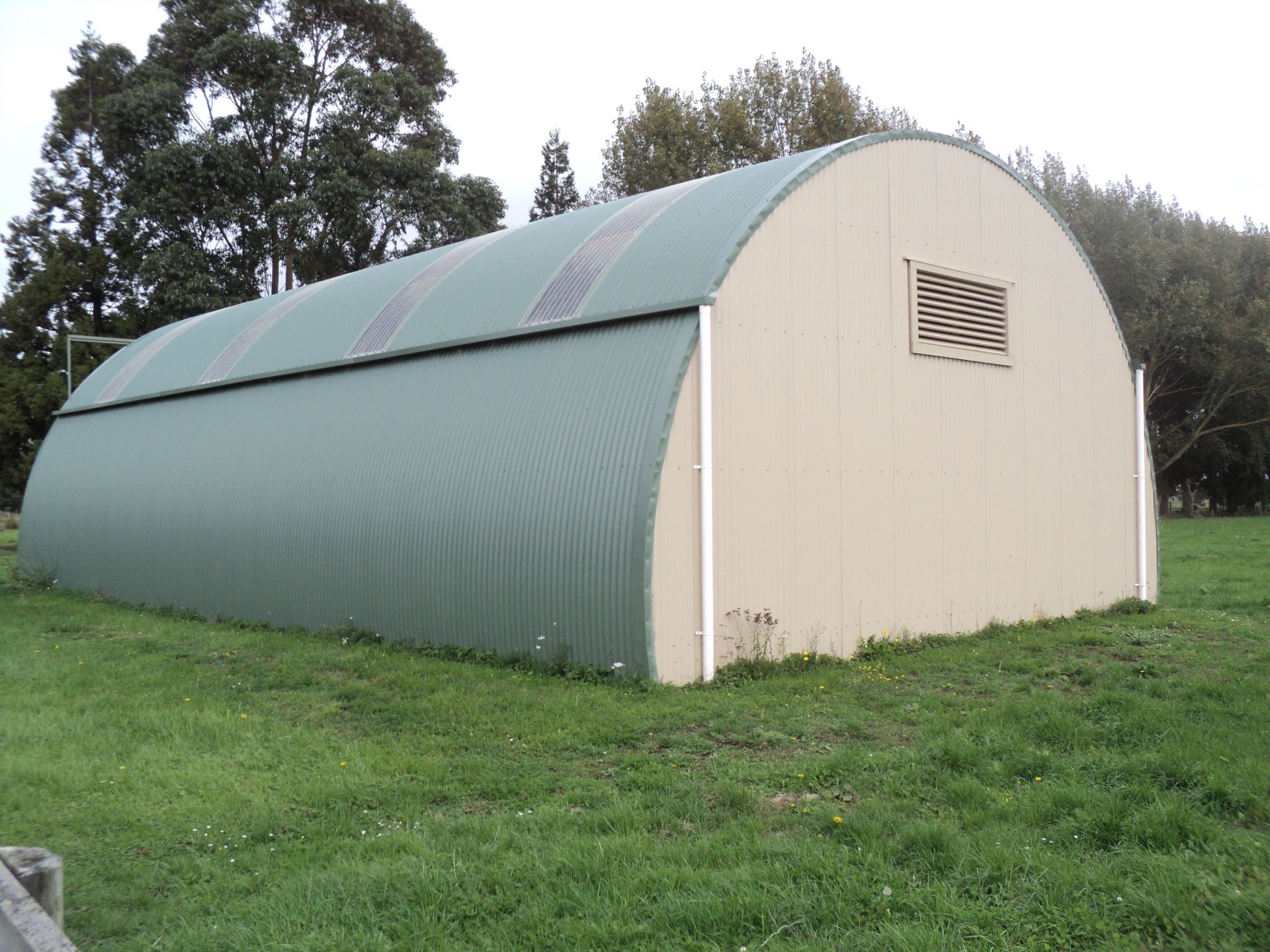 A long building with a clear roof is sitting on top of a gravel road.