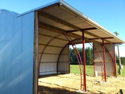 A metal building with a roof is sitting in the middle of a field.