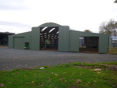 A large green building with a lot of doors is sitting in the middle of a grassy field.