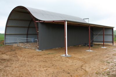 A large metal building with a curved roof is sitting in the middle of a dirt field.