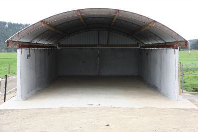 An empty building with a curved roof is sitting in the middle of a field.