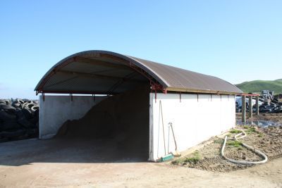 A white building with a brown roof is sitting in the dirt.