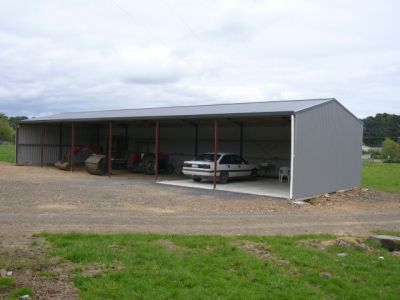 A white car is parked under a shed in a grassy field.