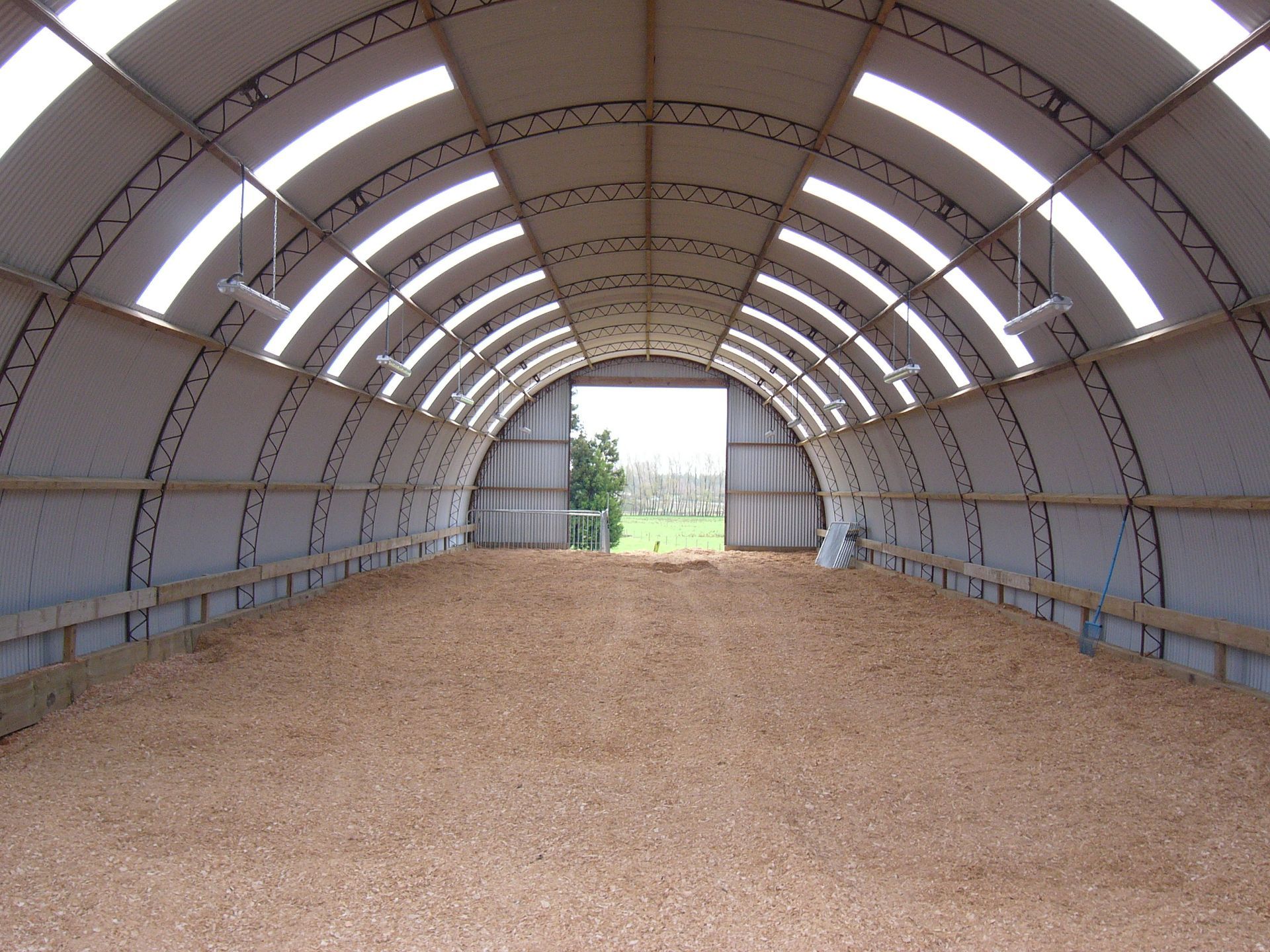 A large green barn with a curved roof is sitting in the middle of a dirt field.
