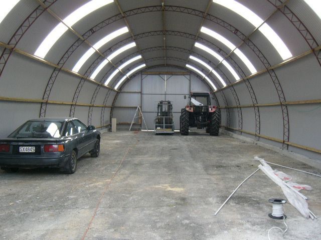 A large green barn with a curved roof and a roller door.