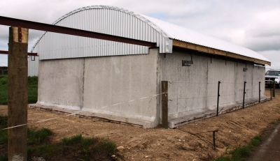 A large concrete building with a white roof is sitting next to a dirt road.
