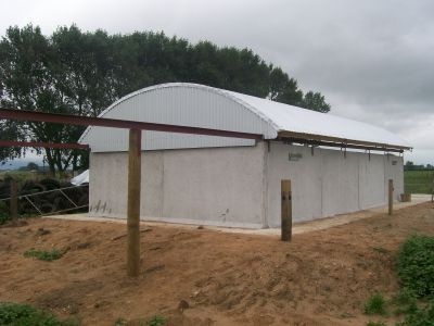 A white building with a curved roof is surrounded by dirt and trees