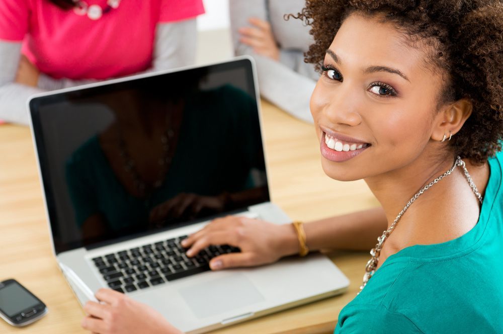 A Woman Is Smiling While Using A Laptop Computer — Lismore Computer Solutions In Lismore, NSW
