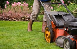 A man is using a lawn mower to cut the grass in a garden.