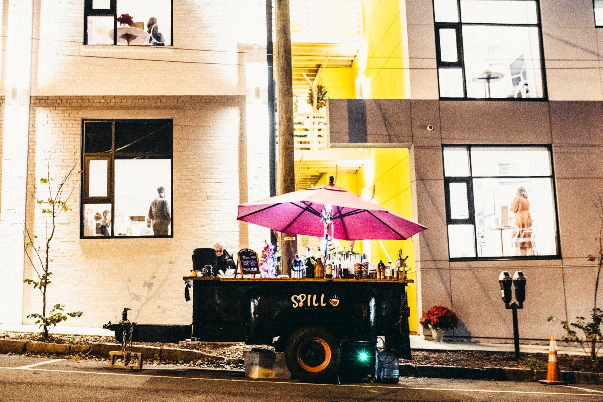 A mobile bar with a pink umbrella is parked in front of a building.