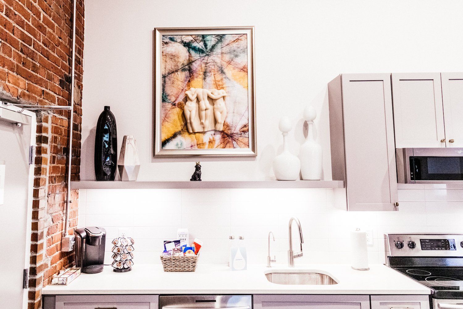 A kitchen with a painting on the wall above the sink.