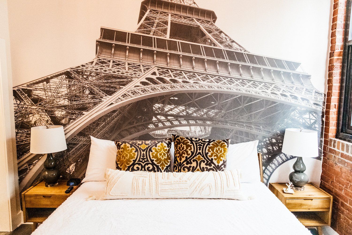 A bed with a picture of the eiffel tower on the wall behind it.