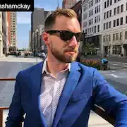 A man in a blue suit and sunglasses is standing in front of a city street.