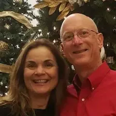 A man and a woman are posing for a picture in front of a christmas tree.