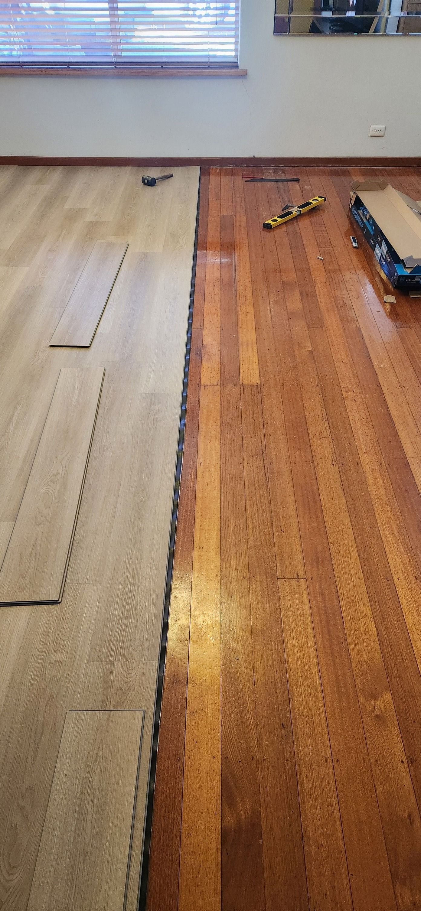 Floor installation in progress; wood flooring next to lighter-coloured flooring. Tools and window in the background — Carro's Property Maintenance in Kaleen, ACT