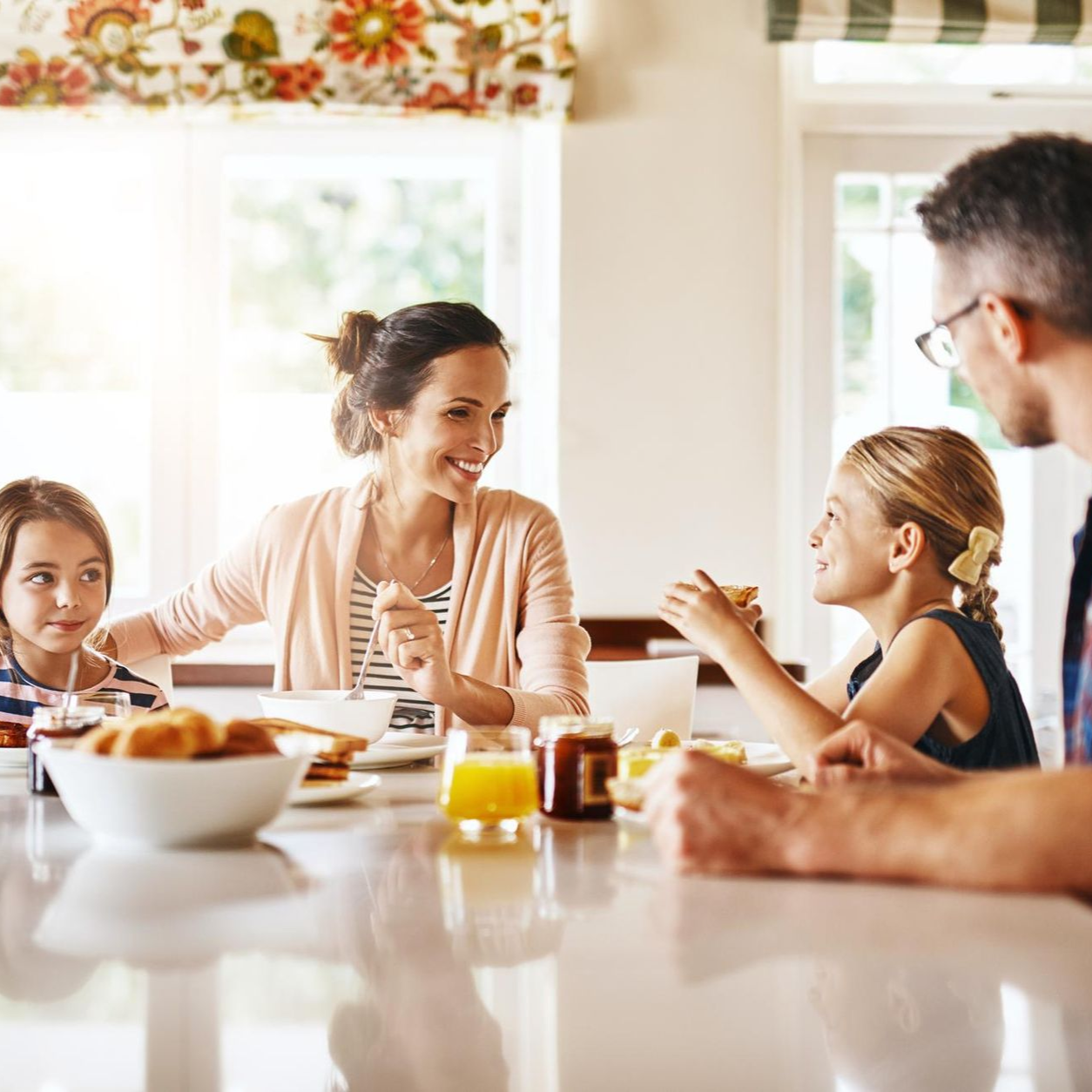 A woman is carrying a little girl on her shoulders in a field at sunset.