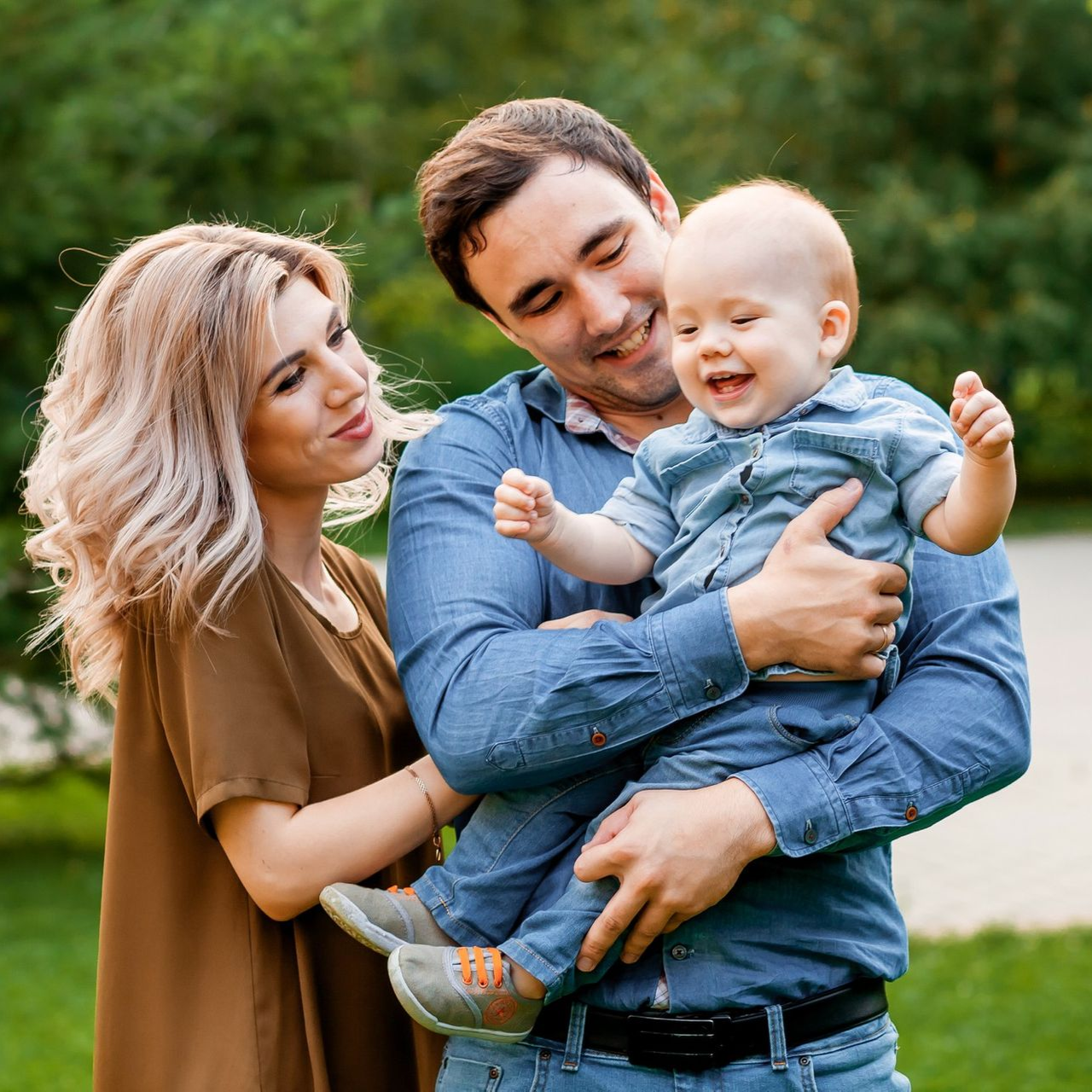 A woman is carrying a little girl on her shoulders in a field at sunset.