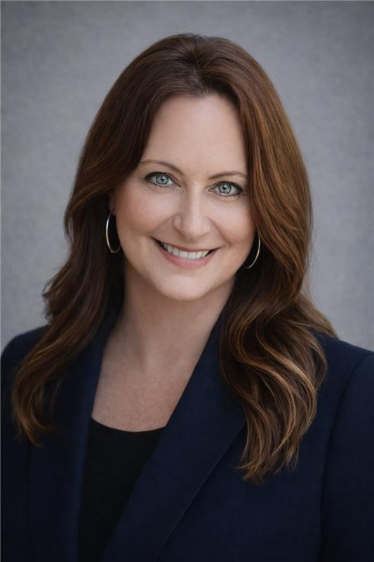 Woman with long brown hair, wearing a navy blazer, smiling, and looking at the viewer.