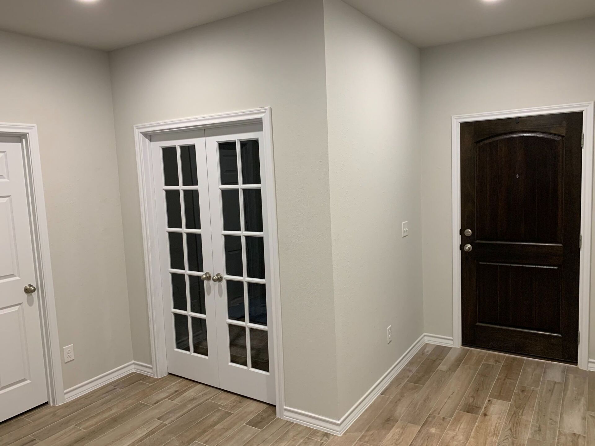 A hallway with french doors and a brown door.