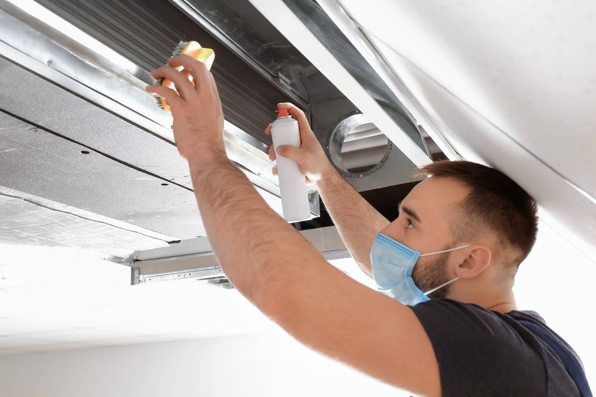 A man wearing a mask is spraying something on a ceiling.