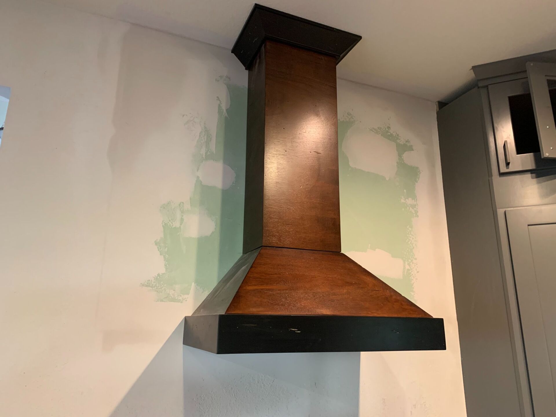 A wooden hood is hanging from the ceiling in a kitchen.