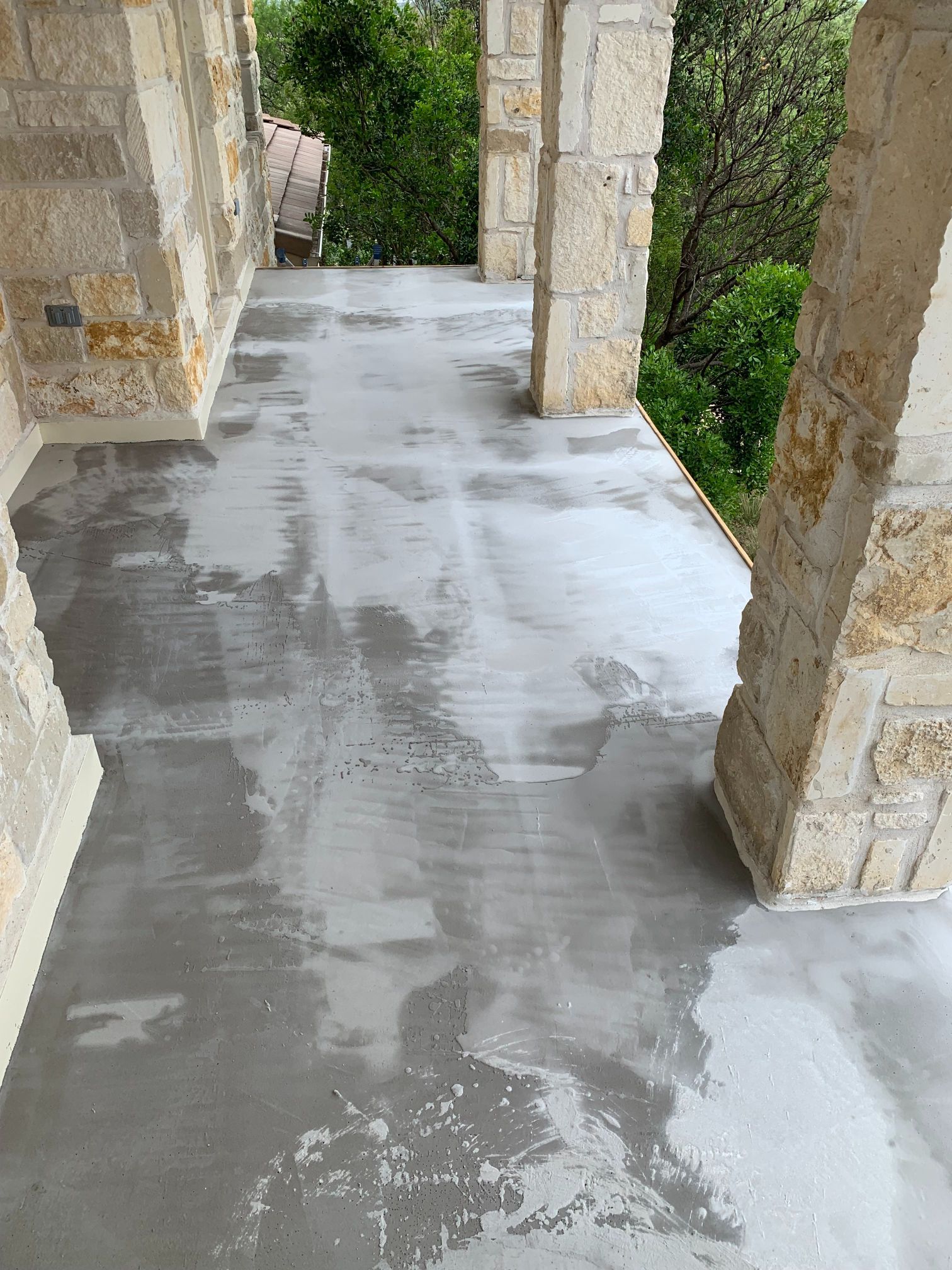 A concrete walkway between two stone pillars with trees in the background.