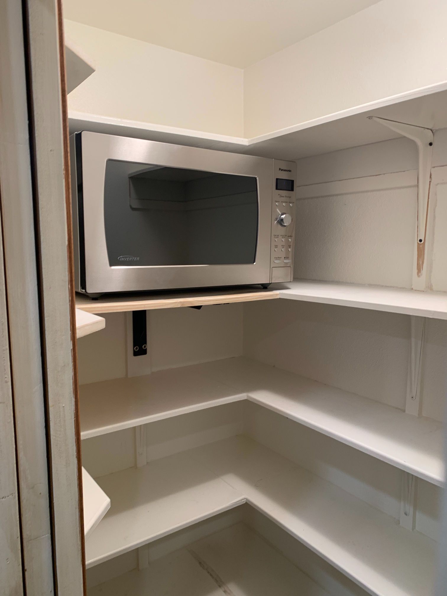 A microwave oven is sitting on top of a shelf in a pantry.