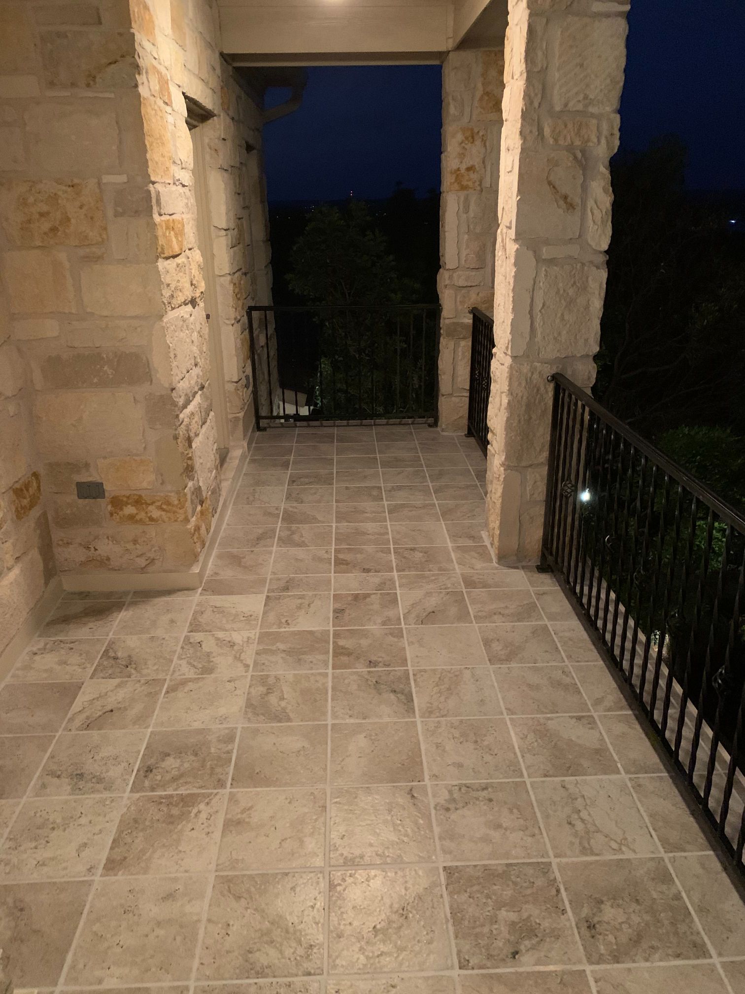 A stone walkway with tile floors and a railing at night.