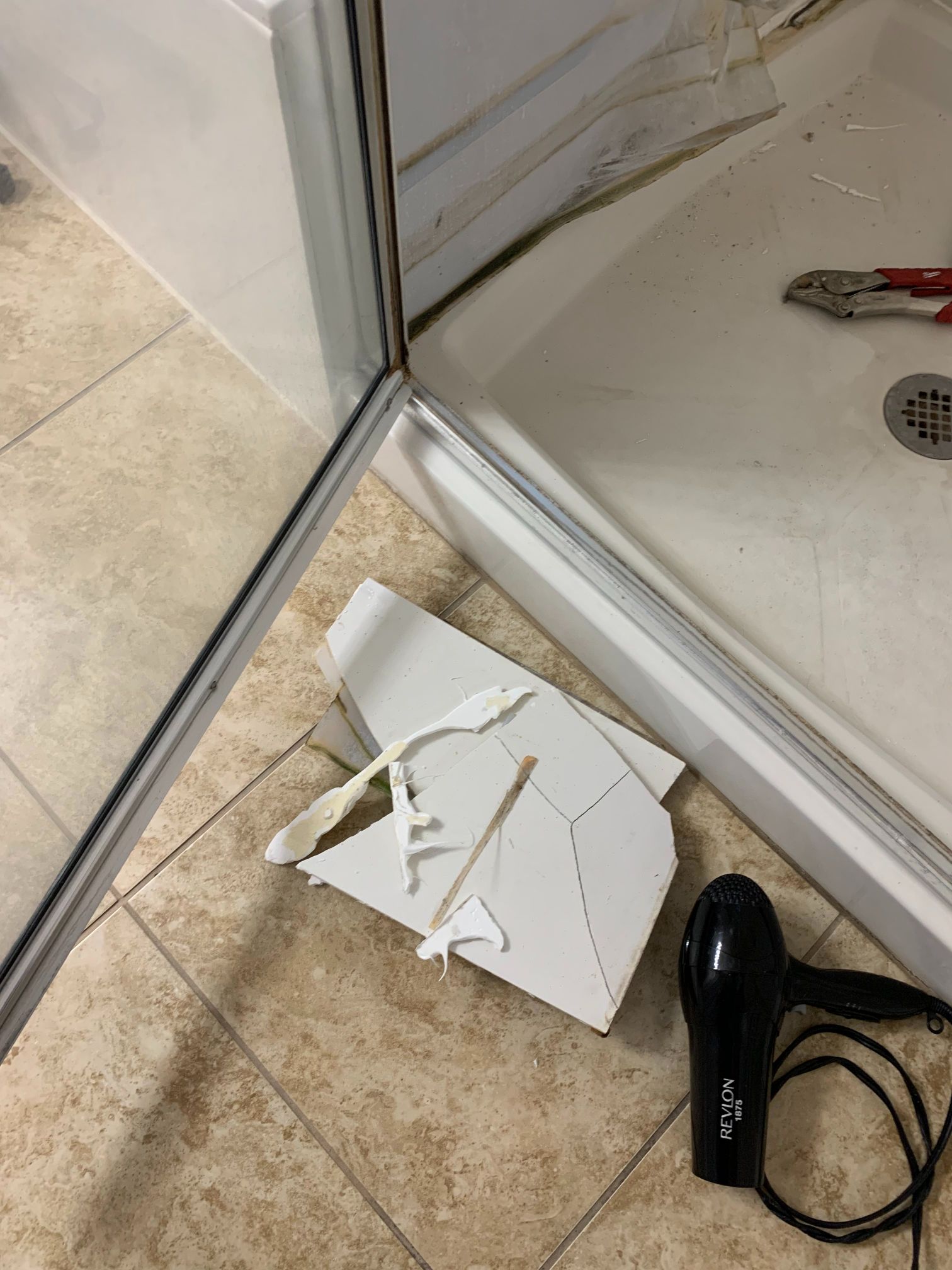 A shower door with a broken piece of plastic on the floor next to a hair dryer.