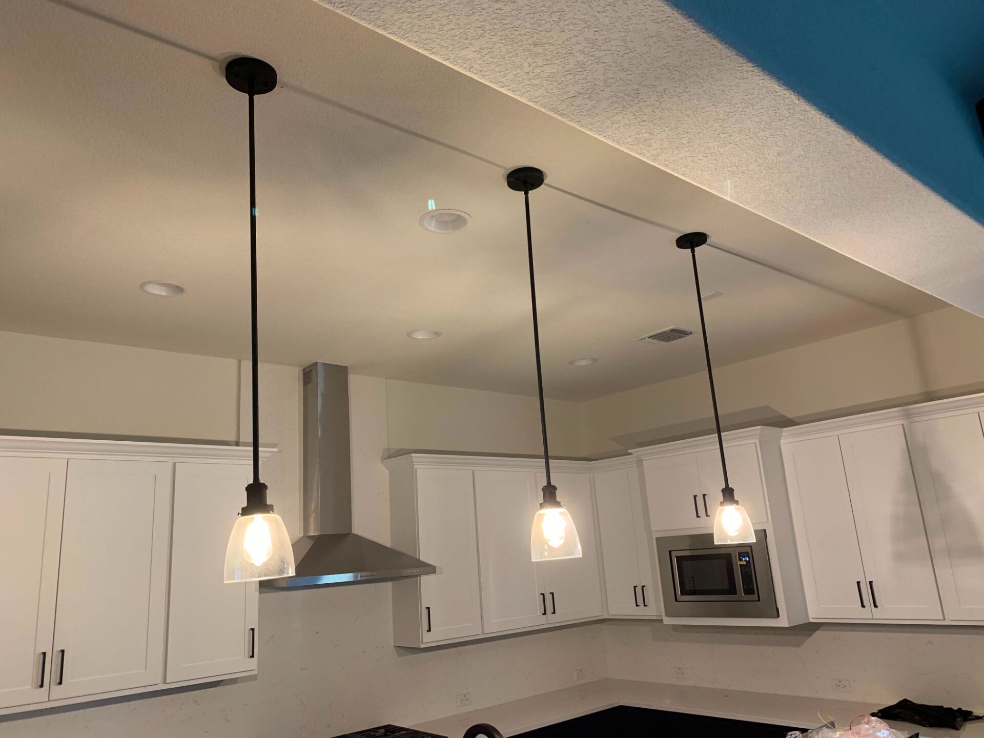 A kitchen with white cabinets and pendant lights hanging from the ceiling