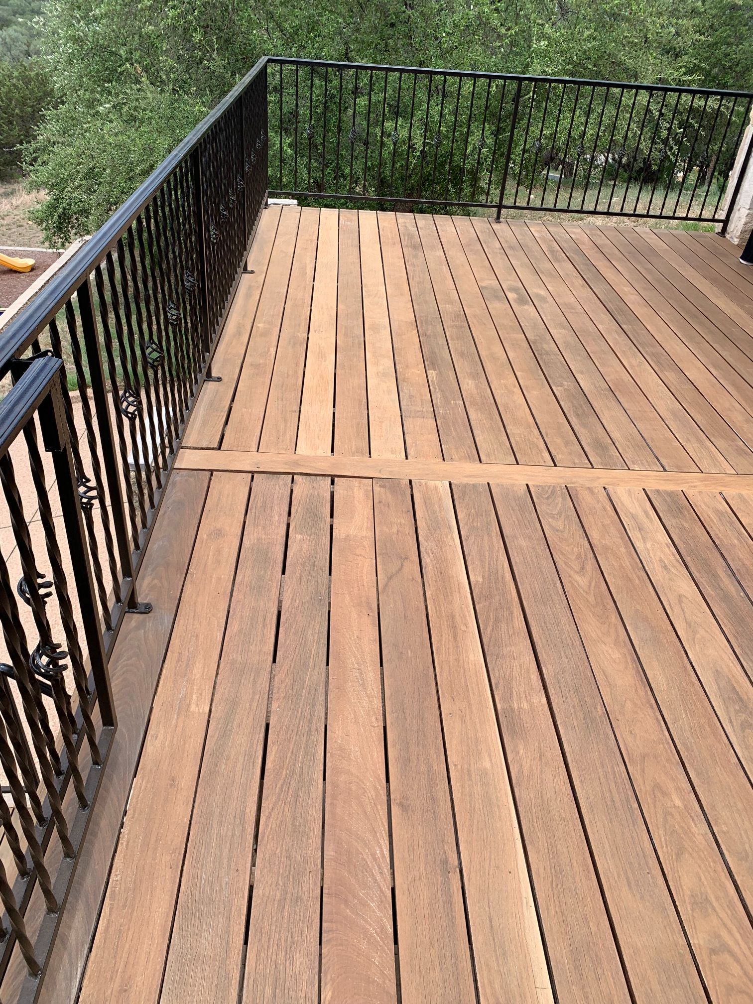 A wooden deck with a metal railing and trees in the background.