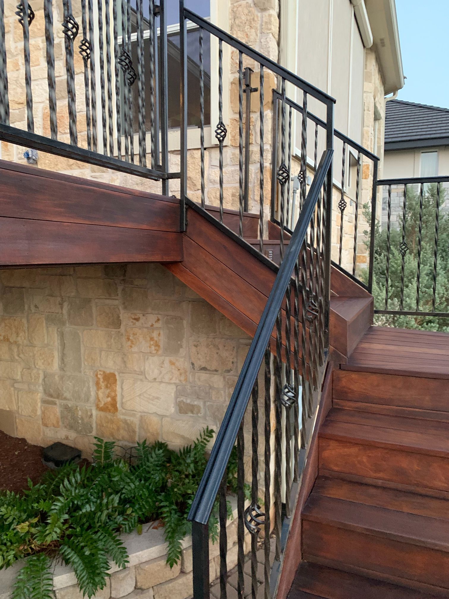A wooden deck with stairs leading up to a house with a wrought iron railing.