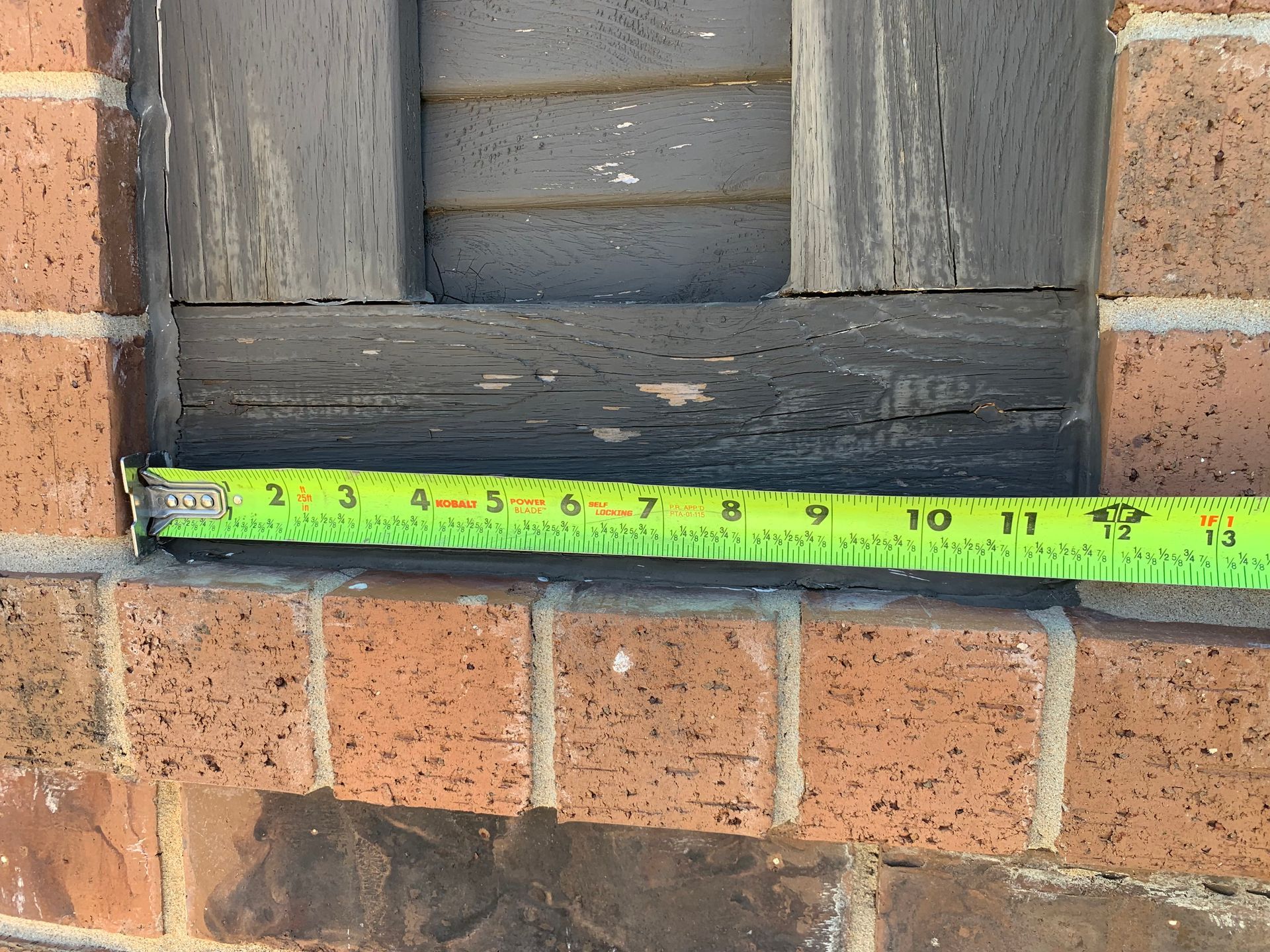 A green tape measure is being used to measure a brick wall