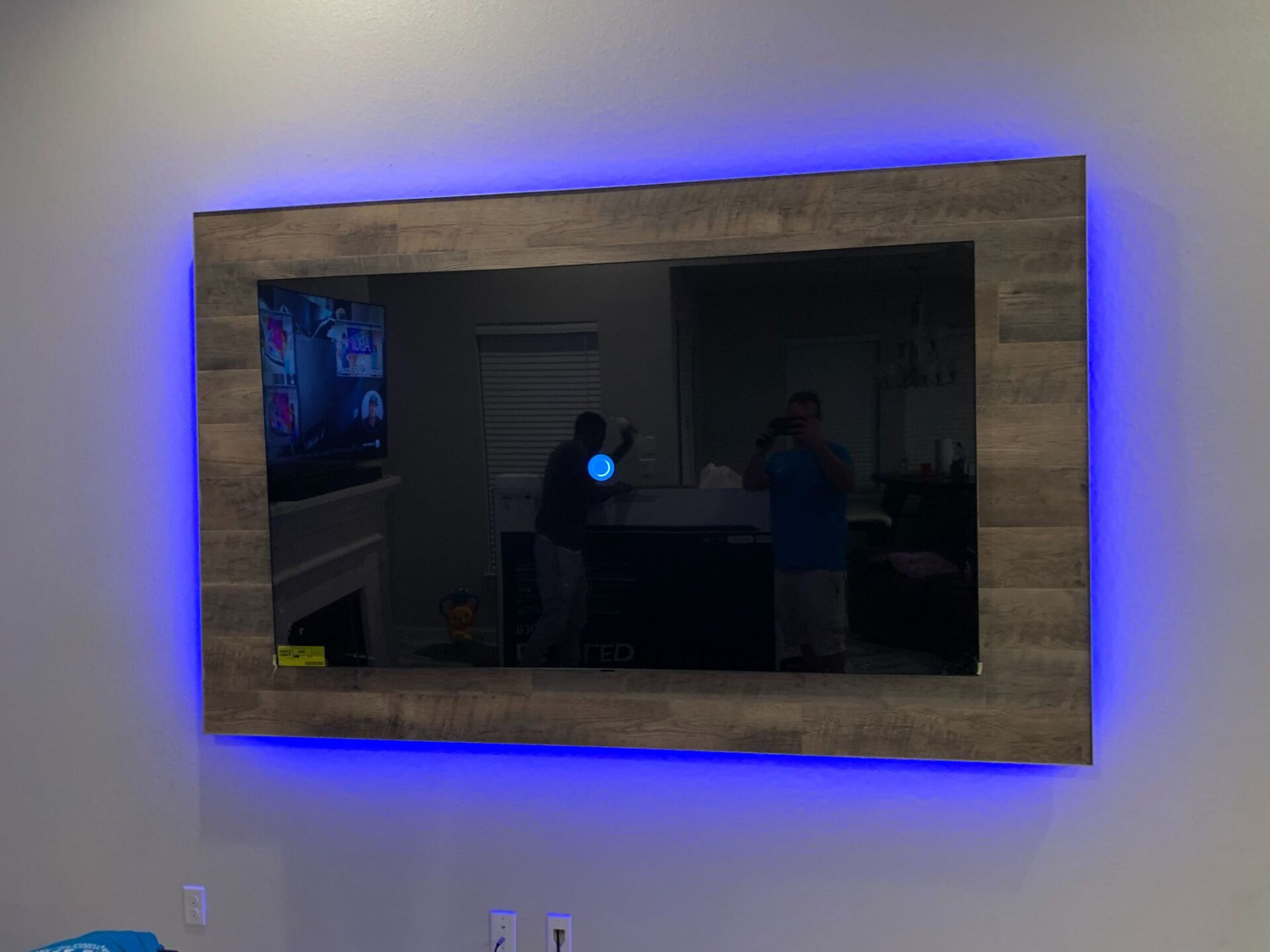 A flat screen tv is hanging on a wall with blue lights around it.