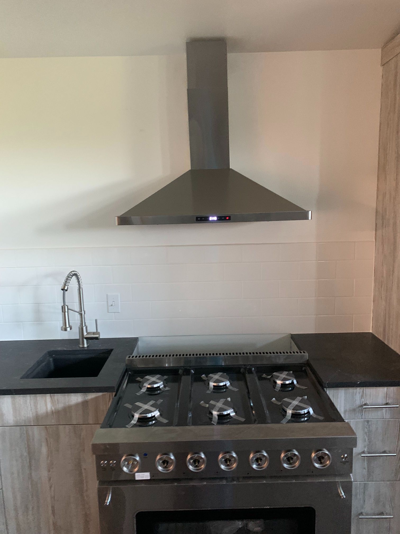 A kitchen with a stove , sink , and hood.